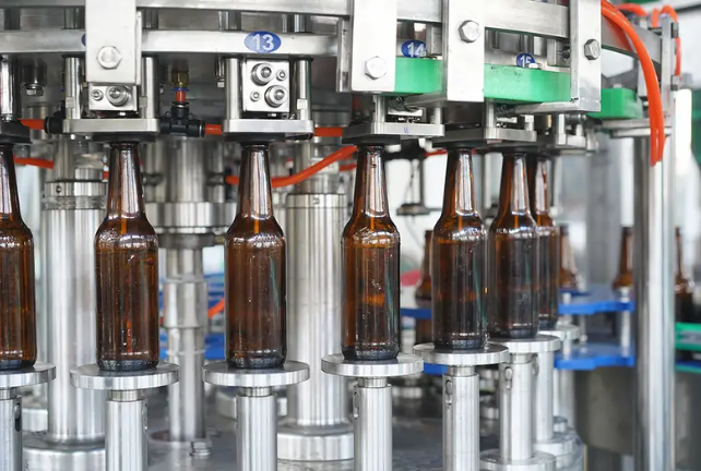 Modern beer filling machine automatically pouring fresh beer into cans on a stainless steel brewery production line.